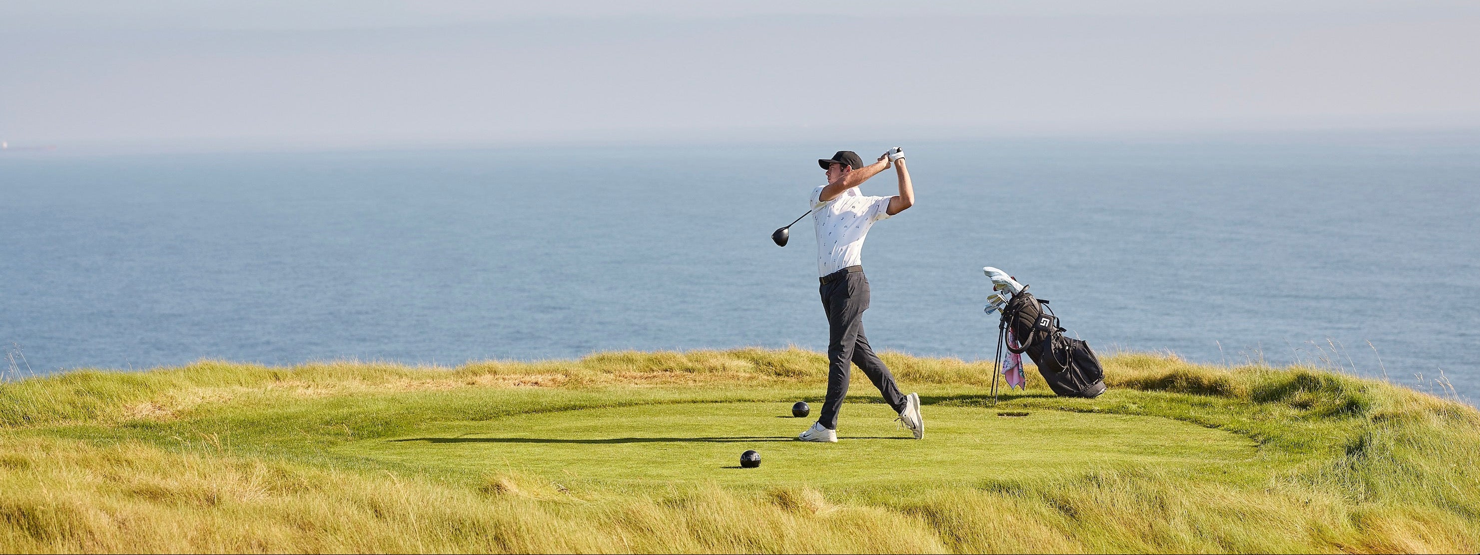 Person playing golf on a grassy area with ocean in the background
